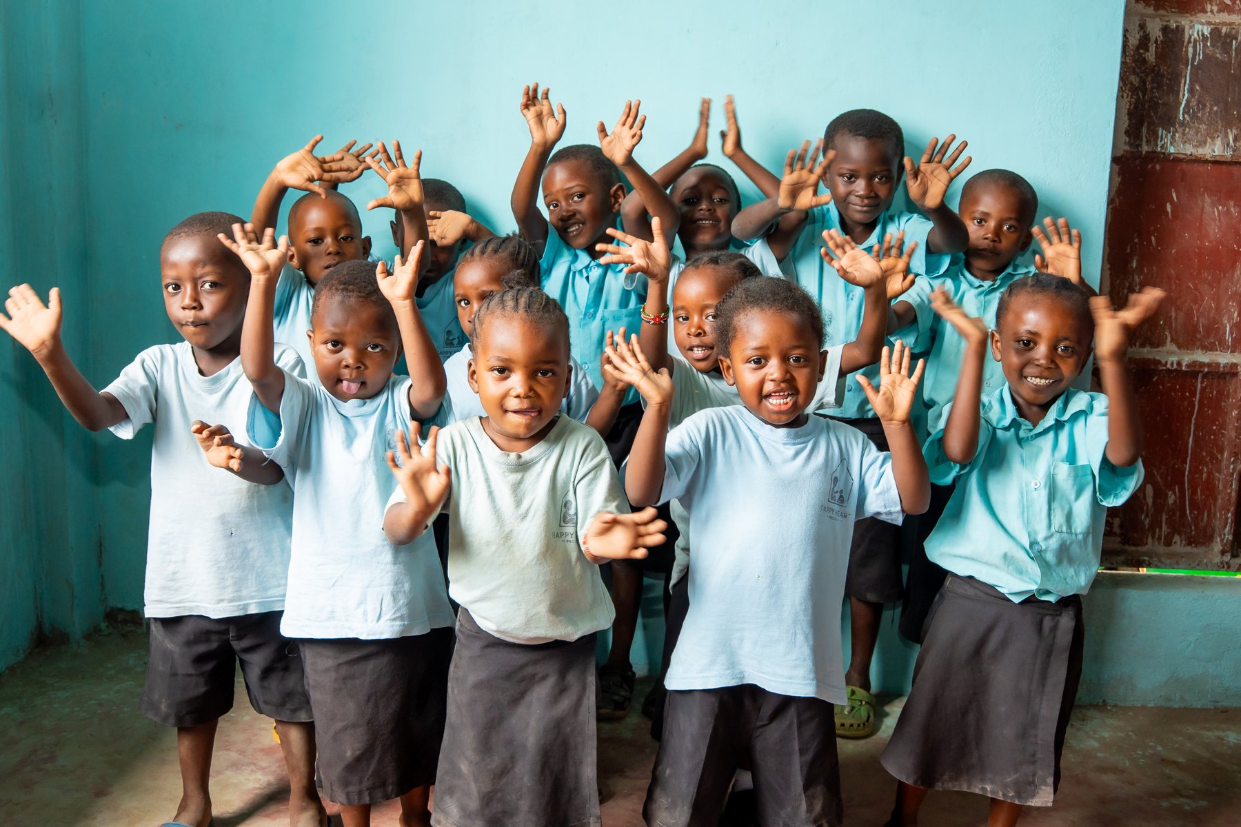 Kinder der Happy Hearts Academy winken in die Kamera.