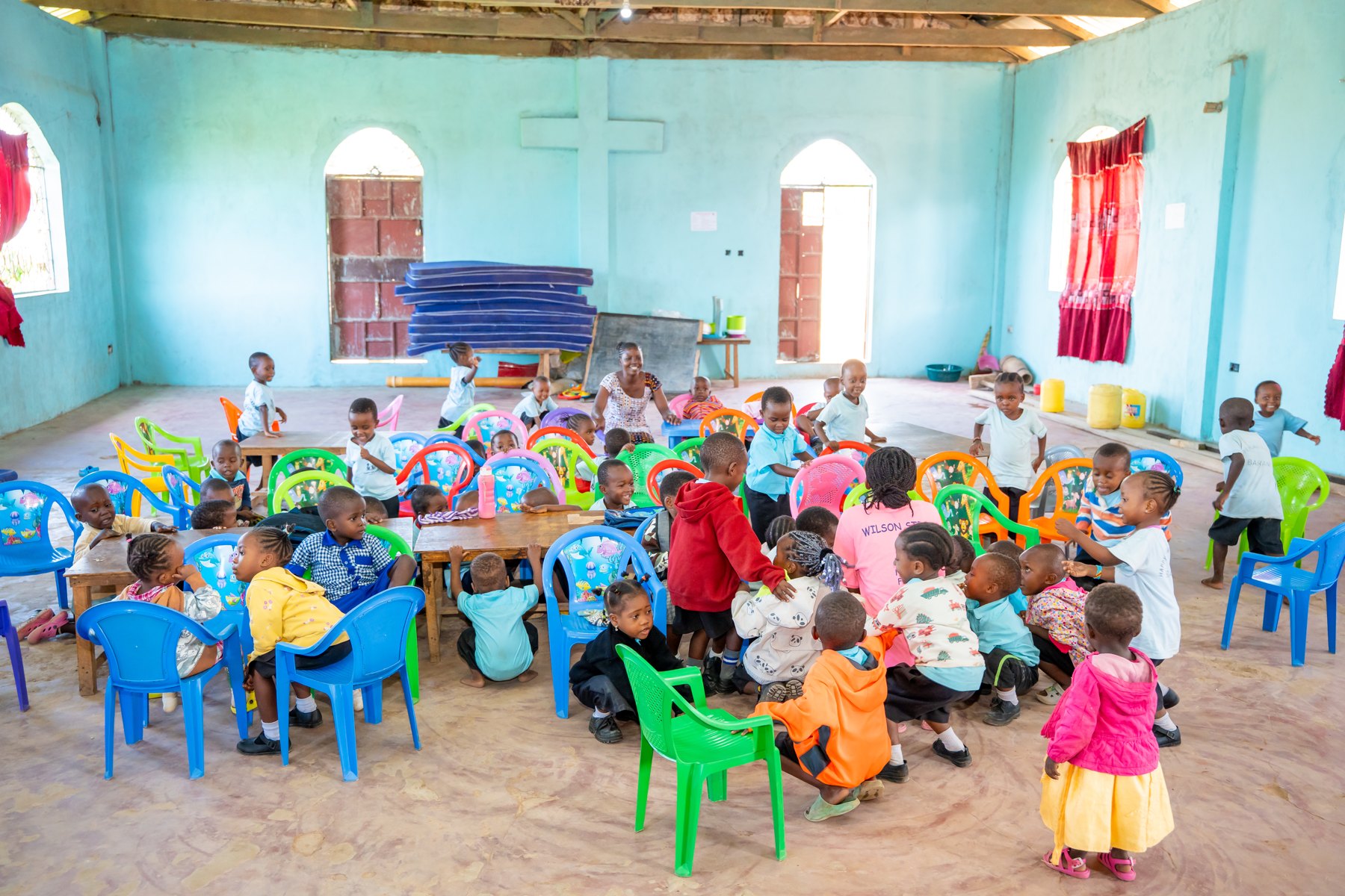 Kinder sitzen gemeinsam an bunten Tischen im Schulraum.